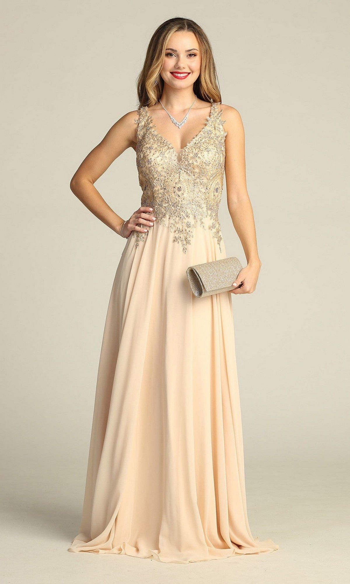 A woman wearing the Chicas DM4006 long formal dress in champagne, which features an intricately embroidered bodice and a flowing chiffon A-line skirt, holds a clutch and smiles at the camera.